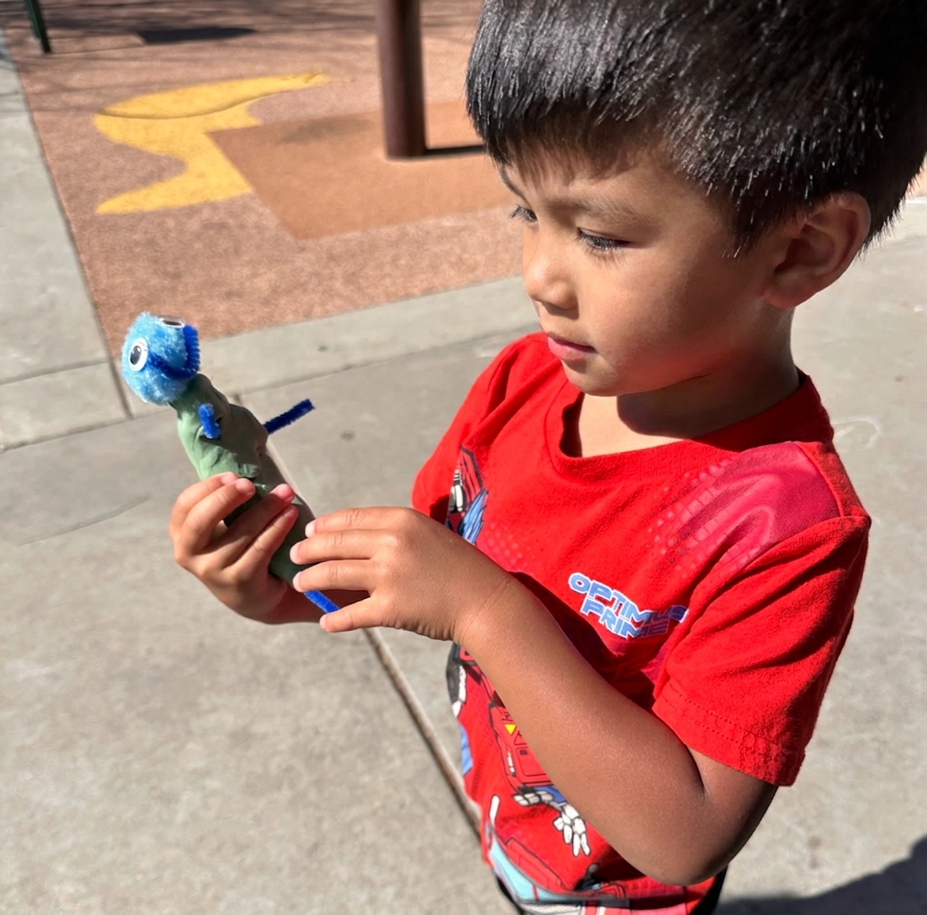 A child holding a small handmade critter with pipe cleaners and a googly eye