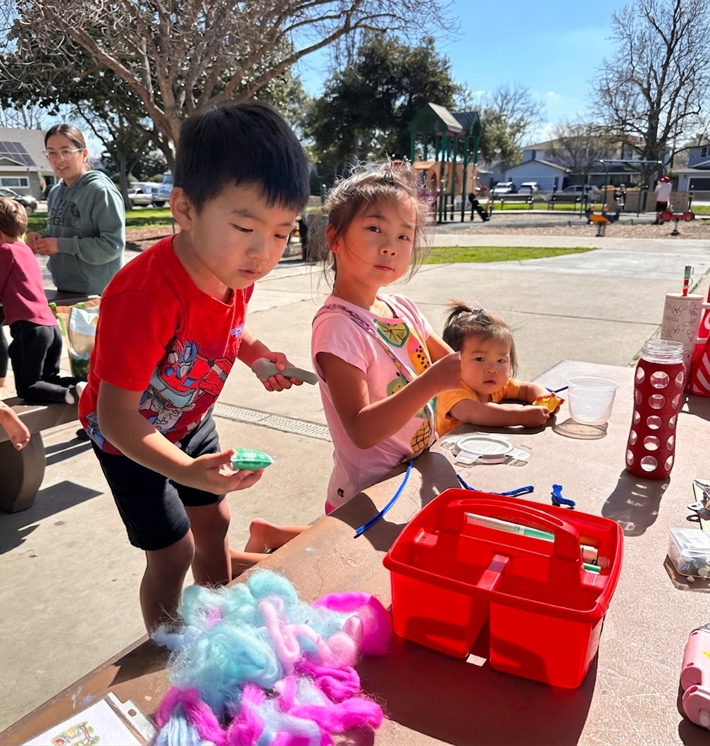 Children gathered around a craft table building their creatures from fiber and craft materials