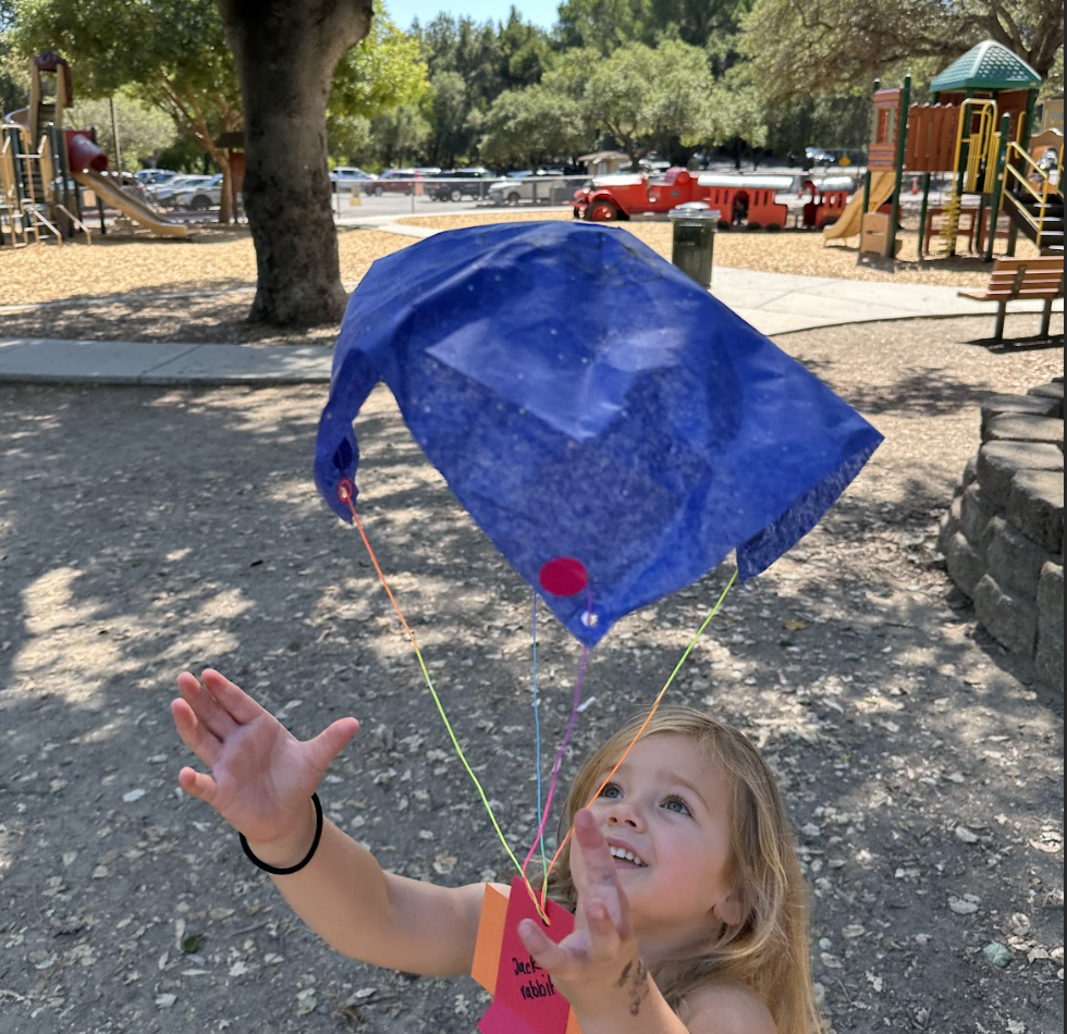 A child carefully adjusting the strings of their tissue paper parachute on the grass.