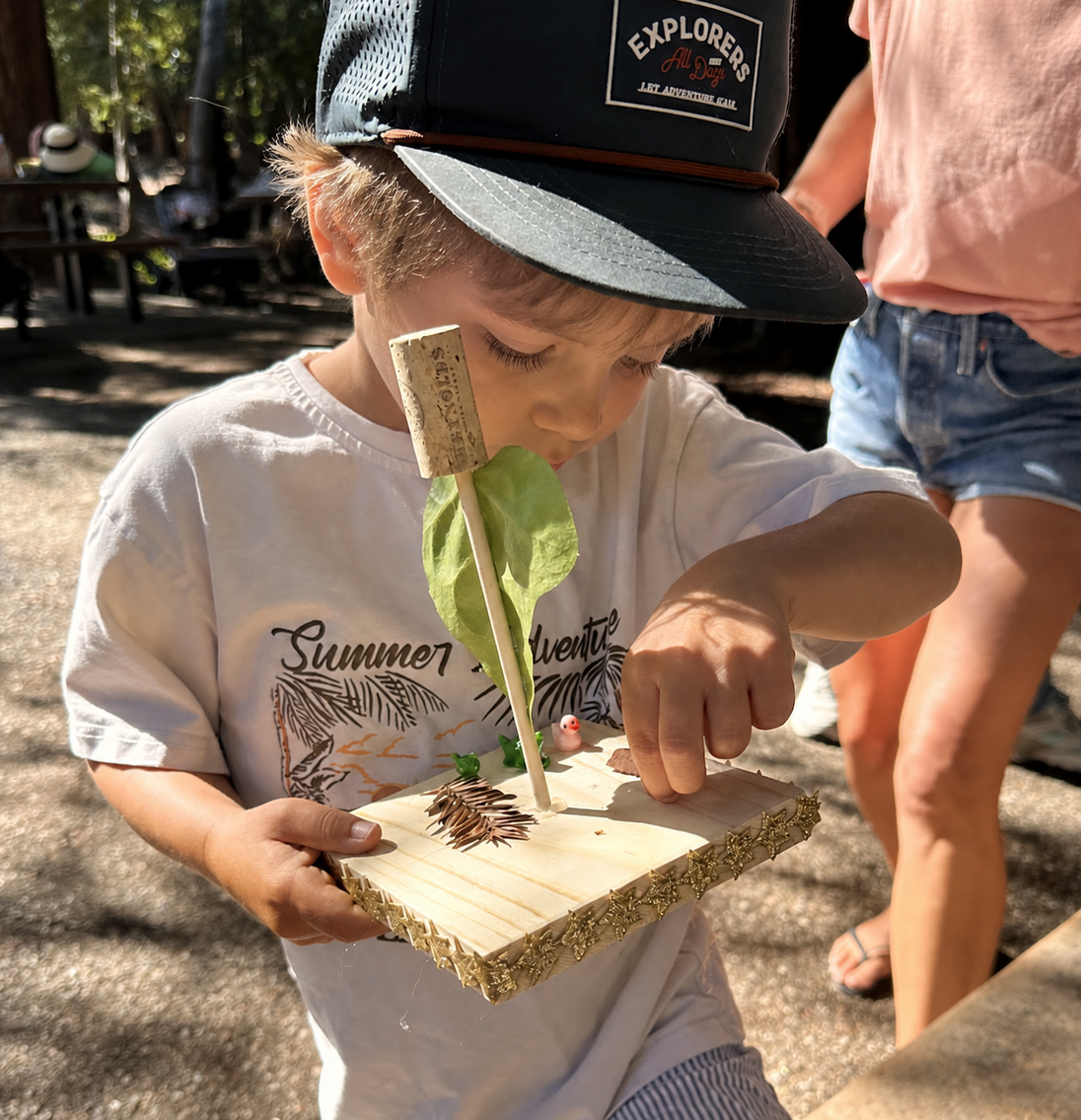 A child carefully attaching a balloon to a straw nozzle on their wooden car chassis.