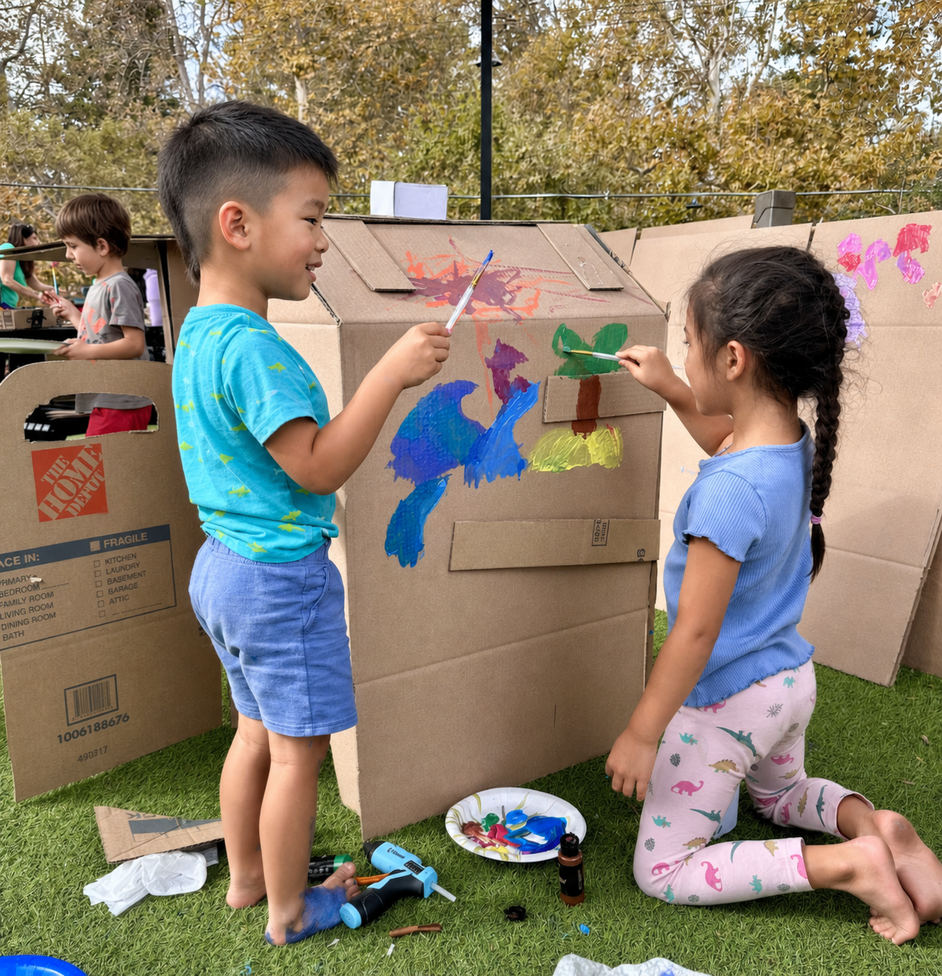 Three children collaborating at a wooden park table, measuring and cutting cardboard to assemble their custom warrior armor.