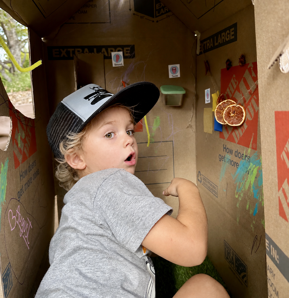 Two children holding a cardboard shield, carefully taping a handle to the back.